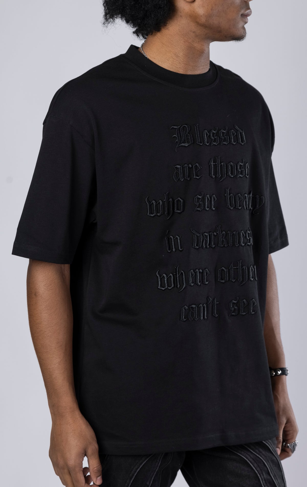 Blessed Darkness Boxy Tee. Black t-shirt made from 100% heavy black 250gr cotton. Features a boxy fit, dropped shoulders, longer sleeves, a 3D embroidered front message, and subtle "blessed" branding